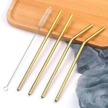 Charger l'image dans la galerie, Set of four gold stainless steel straws with a cleaning brush on a wooden surface.