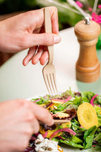 Charger l&#39;image dans la galerie, Main hand holding a reusable 16cm fork, picking salad from a plate, with a wooden pepper grinder in background.