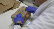 Charger l&#39;image dans la galerie, Person placing a box of eco-friendly bagasse straws on a scale in a workspace with blue gloves.